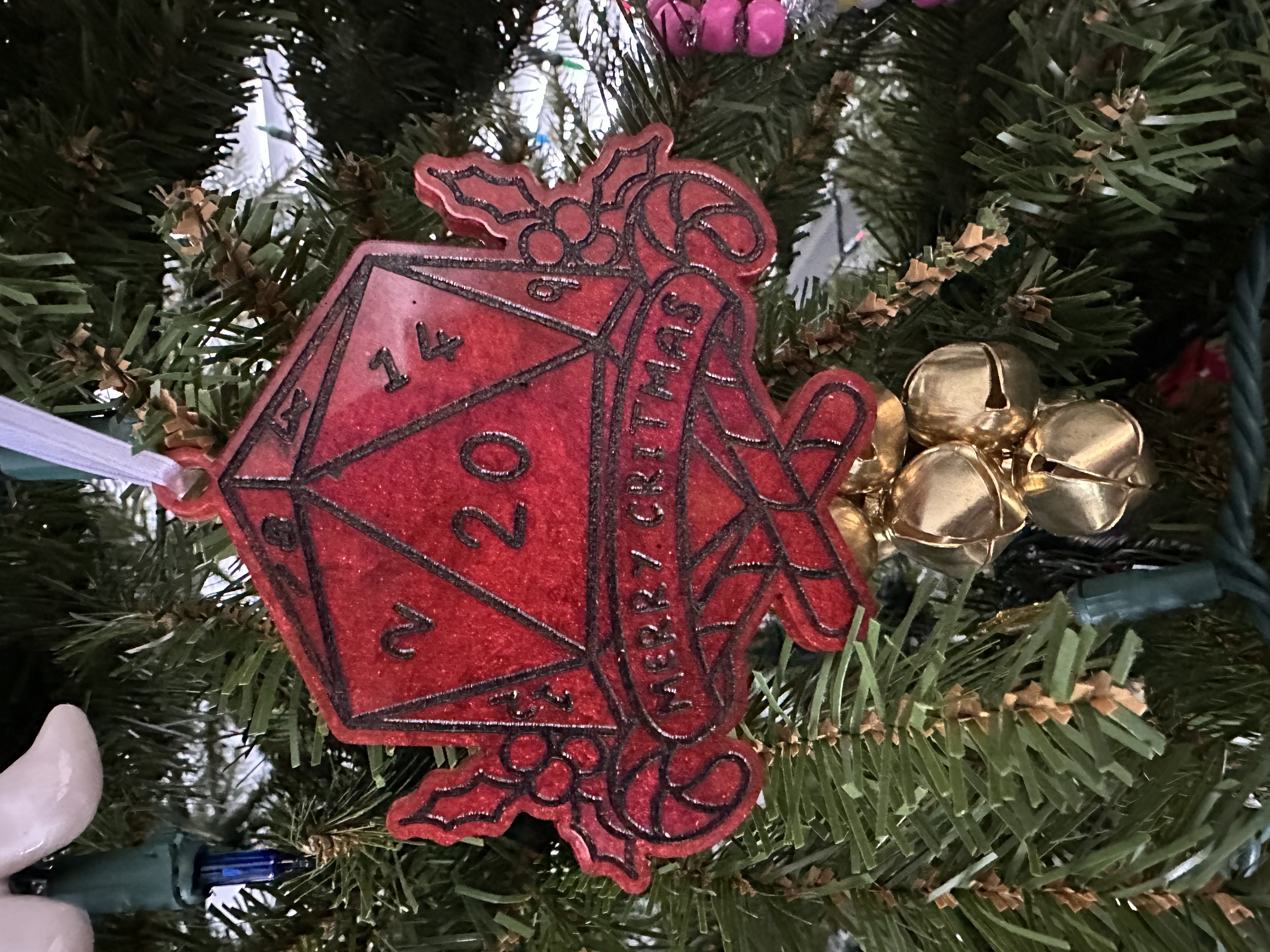 A red Christmas ornament featuring a twenty-sided die, with the 20 face up. A banner underneath reads “Merry Critmas” (as in a critical hit).